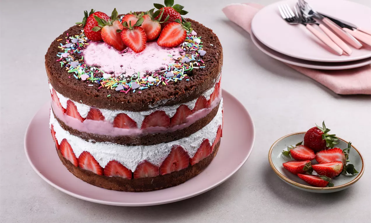 Kakao pandispanya katları arasında krema ve bütün çileklerle süslenmiş, üstünde renkli şekerlemeler ve taze çilekler bulunan pasta