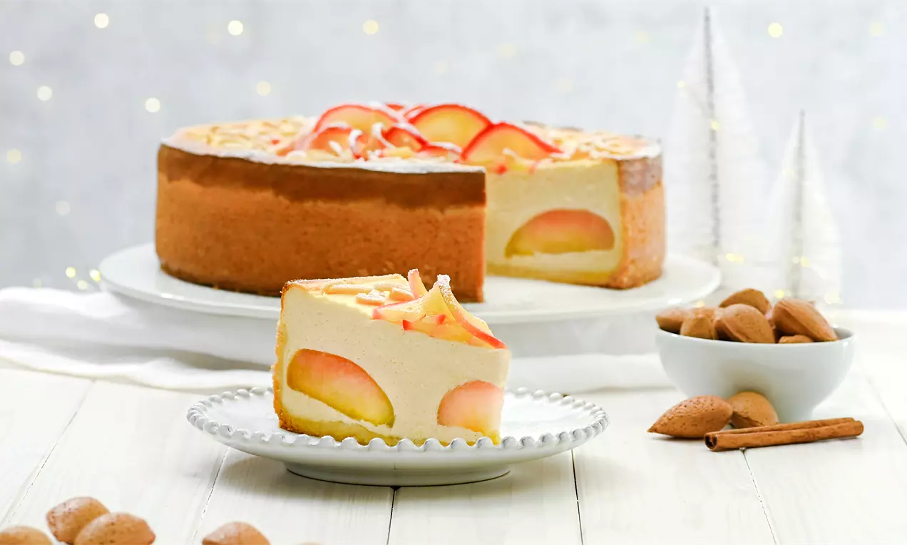 Altın rengi elma dilimleri ve badem parçalarıyla süslenmiş, dolgulu krem peynir katmanlı yuvarlak elmalı cheesecake dilimi