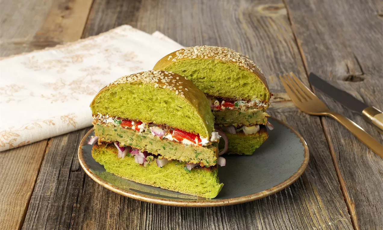 Ispanaklı yumuşak yeşil burger ekmeği arasında nohut köftesi, kıyılmış kırmızı soğan, közlenmiş kırmızı biber ve beyaz peynir dolgulu