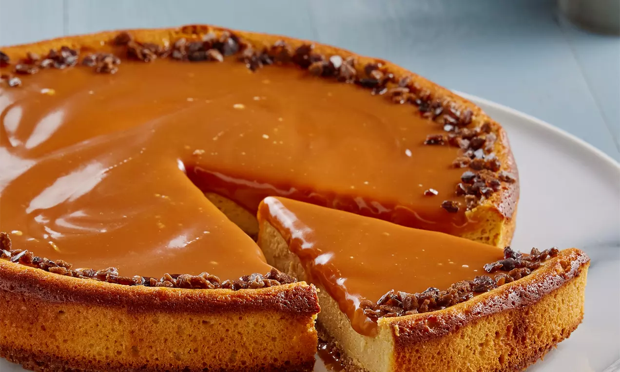 Karamel sosla kaplanmış, kenarları kıtır parçalarla süslenmiş, kremalı dolgusuyla dengelenmiş altın rengi cheesecake beyaz tabakta