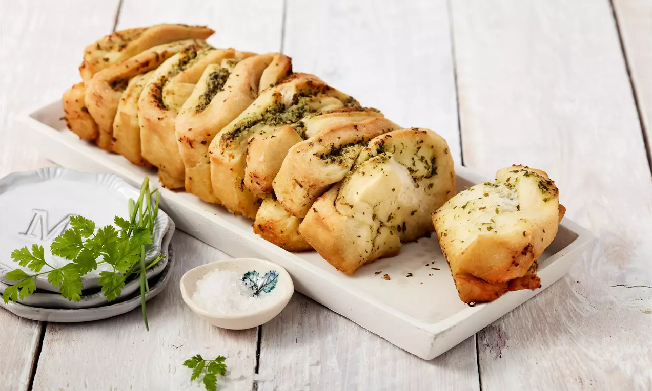 Altın sarısı, yumuşak ve kıtır dokulu, tereyağlı ve otlu dilimler halinde sunulmuş, beyaz ahşap bir tabakta servis edilmiş ekmek